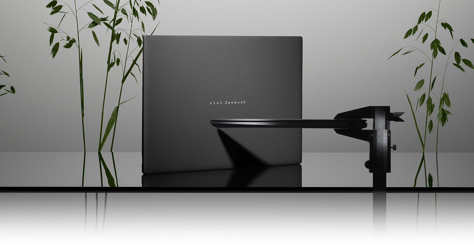 Zenbook S16 na cimnym tle. Na pierwszym planie suwmiarka, która mierzy jego grubość