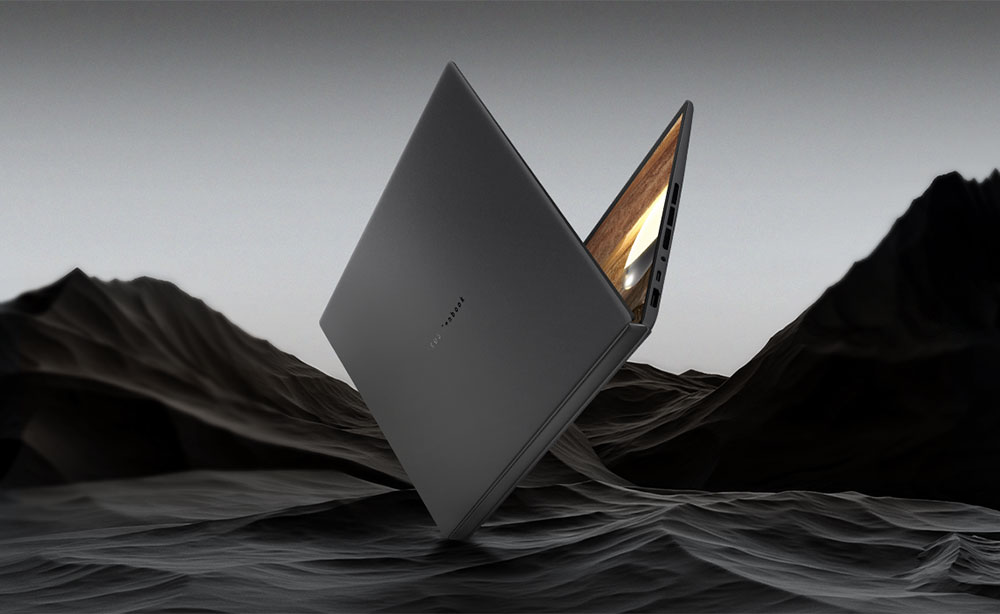 Zdjęcie przedstawia laptopa ASUS w kolorze Moher Grey, ustawionego pod kątem na teksturowanej ciemnej powierzchni przypominającej klify.